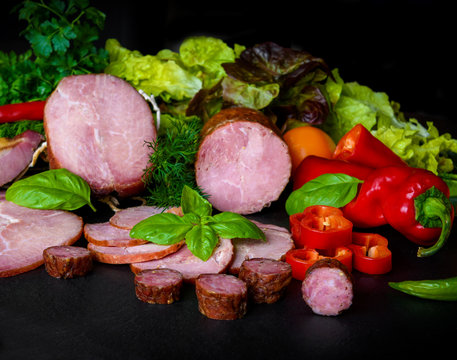 Smoked sausage, ham with red and green peppers and herbs on a dark background