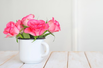 Roses in aged mug on white wooden planks against white wall