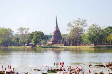 Naklejka premium Ancient buddha statue and pagoda with lotus in the pool at Sukhothai Historical Park, Sukhothai Province, Thailand.