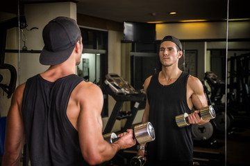 Handsome muscular young man exercising biceps in gym with dumbbells
