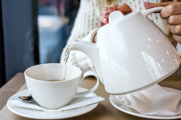 Woman pouring a Cup of hot steaming tea in the restaurant. Winter leisure, cold weather,  drink