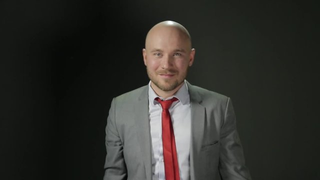 Bald man with a beard in a suit turns to the camera with smiling and Show Big Finger Up. The middle shot. on a black background.