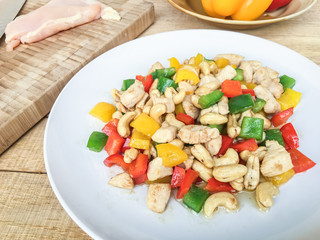 Fried chicken with cashew nuts and bell pepper on white plate on wood table.
