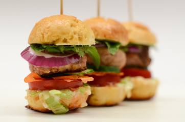 Three tall mini burgers lined up with skewers through middle