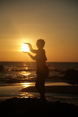 woman on beach holding sun at sunset in silhouette