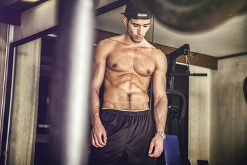 Muscular, shirtless young man resting in gym during workout, showing muscular torso, pecs and abs