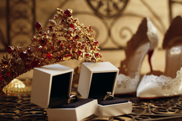 Fototapeta na wymiar Golden crown with red stones, wedding rings and bride's shoes st