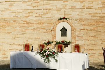 Long table prepared for wedding couple stands before brick wall