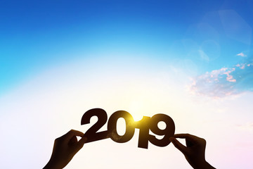 Silhouette hand holding word 2019 with lens flare blue sunset for new year concept.