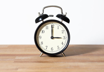 It is three o'clock. The time is 3:00 am or pm. A retro clock isolated on wooden surface. White background. Copy space
