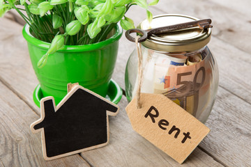 Rental concept - money jar, key with label and little house on the wooden desk
