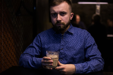 Business man, in blue shirt and glasses, drinking cocktail of vintage old fashion glass in loft bar