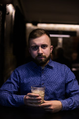 Business man, in blue shirt and glasses, drinking cocktail of vintage old fashion glass in loft bar