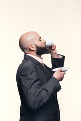 Young bald man with a beard. This guy is standing in profile on a white background while drinking a cup of coffee or tea