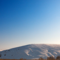 Cloudless blue sky above snow-covered hillside. View at sunset.