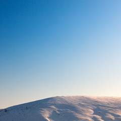 Naklejka na ściany i meble Cloudless blue sky above snow-covered hillside. View at sunset.