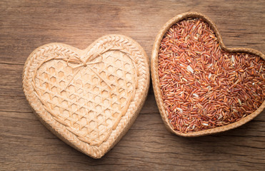 Organic rice grain in heart shape bamboo basket on wooden backgr