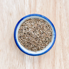 Fennel seed in bowl on wood floor background.