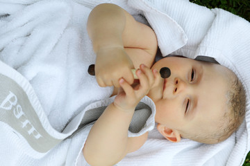 ein Baby liegt , in weisses Tuch gewickelt, auf dem rücken, und versucht ein Spielzeug zu greifen