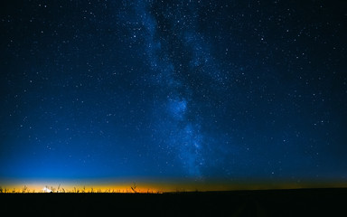 Night Starry Sky Above Field And Yellow City Lights On Background