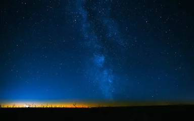 Gordijnen Nachtelijke sterrenhemel boven veld en gele stadslichten op achtergrond © Grigory Bruev