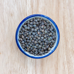 Green lentils in bowl on wood floor background.