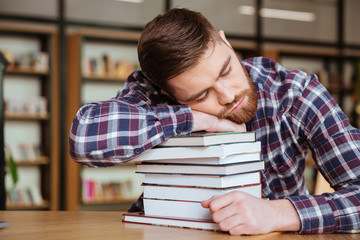 Tired young man holding his head on the book stack