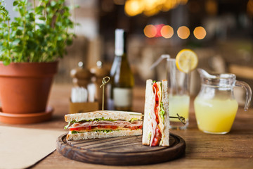 Tasty sandwich with ham, tomato, lettuce, cheese on the wooden plate in the restaurant