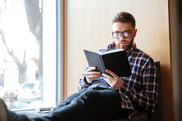 Student sitting on windowsill in library and reading book