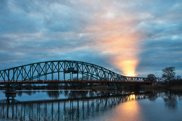 Steel bridge over the river. The light piercing through the clouds.