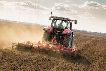 Fototapeta premium Farmer in tractor preparing land with seedbed cultivator