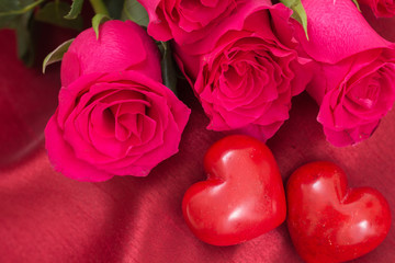 Closeup of red two hearts and roses bouquet, on red fabric background.