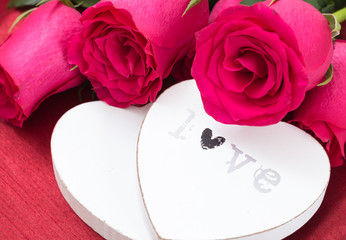 Closeup of two white wooden hearts and roses bouquet, on red fabric background.