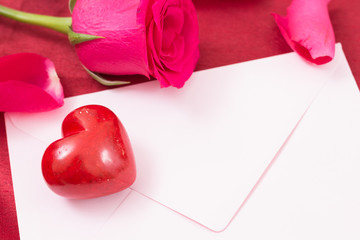 Red heart with pink envelope and red rose and petals closeup.
