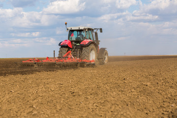 Fototapeta premium Farmer in tractor preparing land with seedbed cultivator