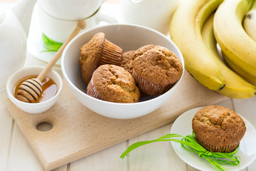 Tea time: homemade banana muffins, honey, bananas and tea settings on white wooden table. Selective focus