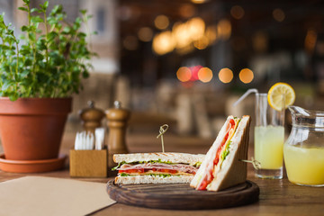 Big, tasty sandwich with ham, tomato, lettuce, cheese on the wooden plate in the restaurant