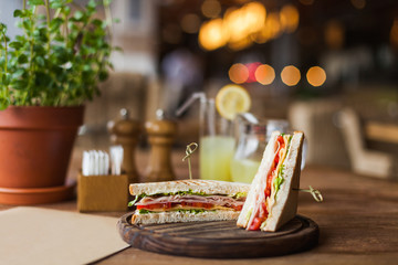 Appetizing sandwich with ham, tomato, lettuce, cheese on the wooden plate in the restaurant