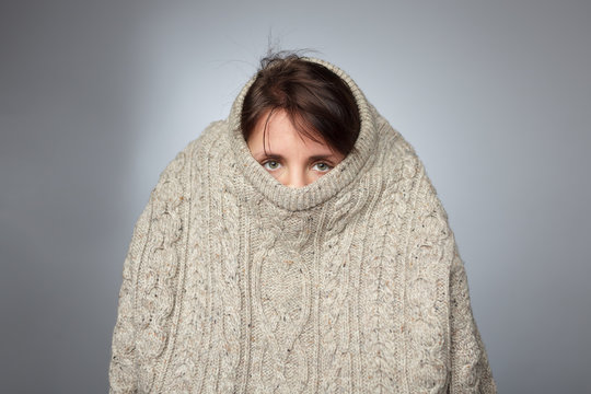 Girl pulls a large knitted sweater over her head. 
