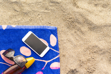 A bottle of sunscreen on a beach towel with mobile phone