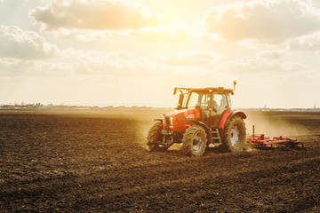 Fototapeta premium Farmer in tractor preparing land with seedbed cultivator as part of pre seeding activities in early spring season of agricultural works at farmlands.