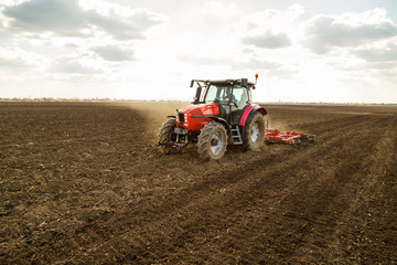 Fototapeta premium Farmer in tractor preparing land with seedbed cultivator as part of pre seeding activities in early spring season of agricultural works at farmlands.