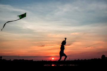 Silhouette girl flying a kite in sunset background.