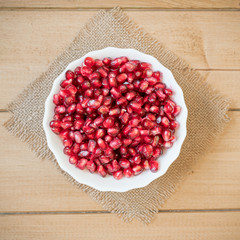 Pomegranate seeds in a bowl on a wooden table.