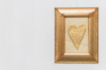 Gold heart in frame on white wooden background. Copy space.