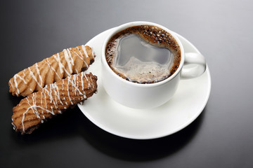 white cup of black coffee with biscuits on a dark background