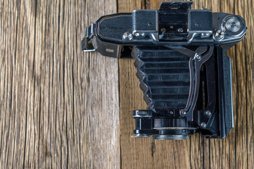 old folding camera on a textured rustic wooden surface.