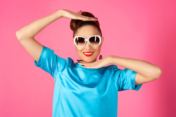 portrait of shocked and surprized young beautiful woman in blue silk dress and white sunglasses ot the pink background