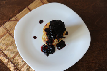 Homemade sweet pancakes with fruit jam on a white plate, top view with copy space