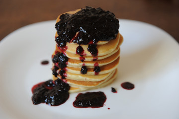 Homemade sweet pancakes with berry jam on a white plate, close up